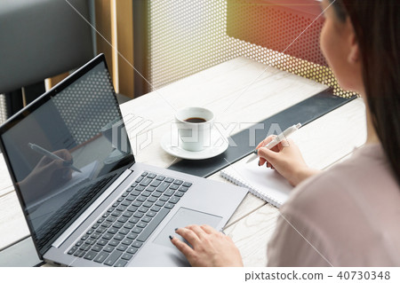 Close up portrait of a young woman working on laptop and writing, coffee on the table. 40730348