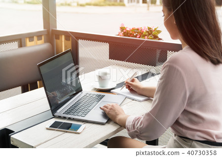 Close up portrait of a young woman working on laptop and writing, coffee on the table. 40730358