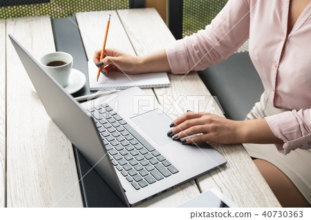 Close up portrait of a young woman working on laptop and writing, coffee on the table. Close up portrait of a young woman working on laptop and writing, coffee on the table. 40730363