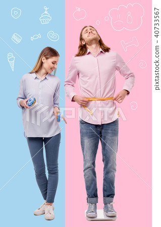 Desperate man being on a diet while his girlfriend eating sweets Desperate man being on a diet while his girlfriend eating sweets 40733567