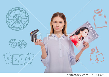 Beautiful woman frowning while standing with a game console and a magazine 40733739