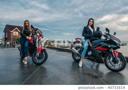 Two Biker girls in leather jackets on a black and red color sport motorcycles Two Biker girls in leather jackets on a black and red color sport motorcycles 40733819