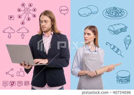 Serious housewife holding a rolling pin and looking at her working husband 40734096