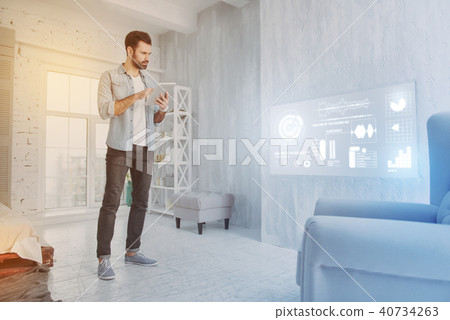 Calm blogger standing with a tablet and looking serious Calm blogger standing with a tablet and looking serious 40734263