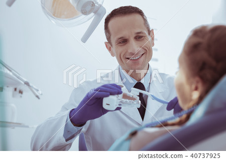 Jolly male dentist demonstrating teeth cleaning on model 40737925