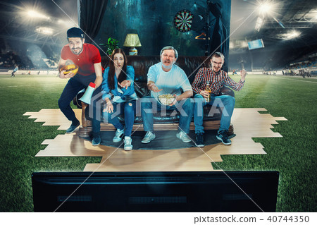 Soccer football fans sitting on the sofa and watching TV in the middle of a football field. Soccer football fans sitting on the sofa and watching TV in the middle of a football field. 40744350