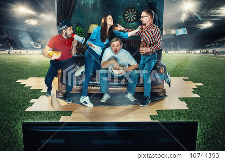 Soccer football fans sitting on the sofa and watching TV in the middle of a football field. Soccer football fans sitting on the sofa and watching TV in the middle of a football field. 40744393