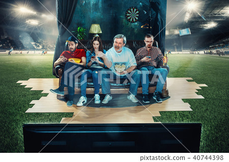 Soccer football fans sitting on the sofa and watching TV in the middle of a football field. Soccer football fans sitting on the sofa and watching TV in the middle of a football field. 40744398