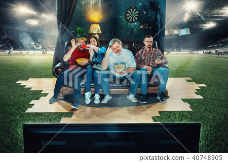 Soccer football fans sitting on the sofa and watching TV in the middle of a football field. 40748905