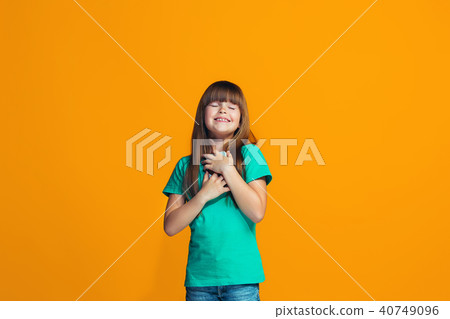 The happy teen girl standing and smiling against orange background. 40749096