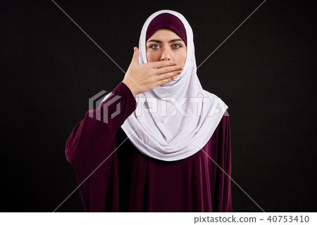 Arab woman in hijab covers mouth with palm. 40753410