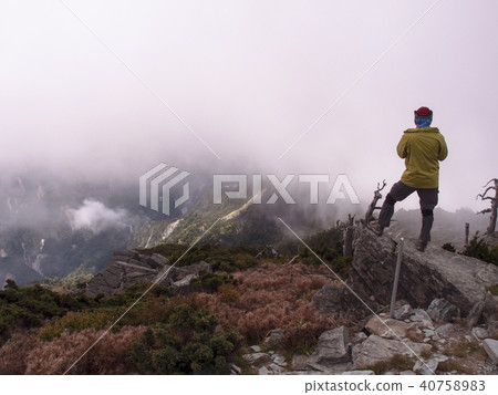 一位男性登山客,停留在山邊的岩石上, 欣賞眼前雲霧繚繞的高山美景 40758983