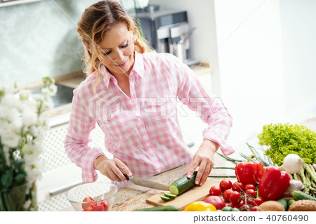 smiling woman is slicing cucumber on a kitchen table 40760490