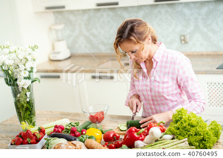 smiling woman is slicing cucumber on a kitchen table 40760495