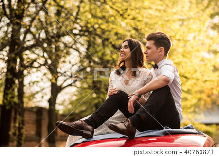 Merry happy young couple sit on the roof of the car. Close-up. Merry happy young couple sit on the roof of the car. Close-up. 40760871