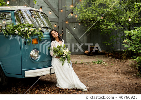 Cheerful happy young bride sit on the bumper retro-minibus. Close-up. Cheerful happy young bride sit on the bumper retro-minibus. Close-up. 40760923
