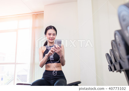 Asian woman using smartphone in fitness gym. Asian woman using smartphone in fitness gym. 40773102