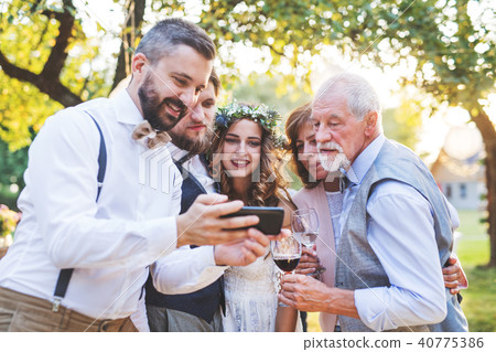 Bride, groom and guests with smartphones taking selfie outside at wedding reception. 40775386