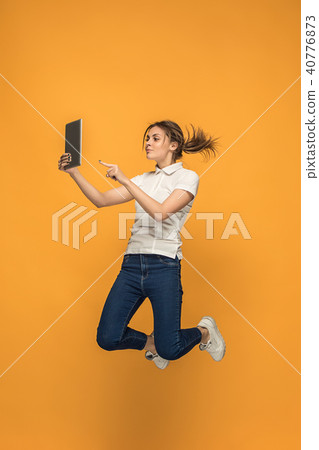 Image of young woman over orange background using laptop computer or tablet gadget while jumping. Image of young woman over orange background using laptop computer or tablet gadget while jumping. 40776873