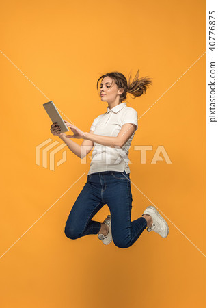 Image of young woman over orange background using laptop computer or tablet gadget while jumping. Image of young woman over orange background using laptop computer or tablet gadget while jumping. 40776875