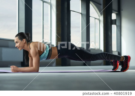 Sporty woman with strong body making plank exercises on gym floor. 40801919