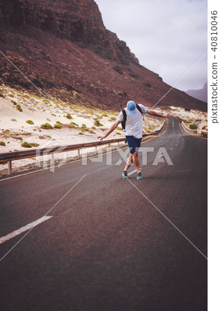 Traveler with backpack standing in the center of an epic winding road. Huge volcanic mountains in Traveler with backpack standing in the center of an epic winding road. Huge volcanic mountains in 40810046