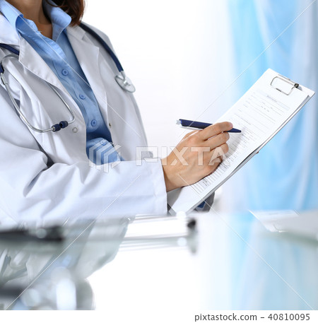 Female doctor filling up medical form on clipboard, closeup. Reflecting glass table is a physician 40810095
