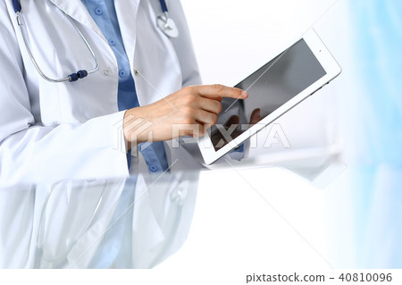 Woman doctor using tablet computer while sitting. Reflecting glass table is a working place of Woman doctor using tablet computer while sitting. Reflecting glass table is a working place of 40810096
