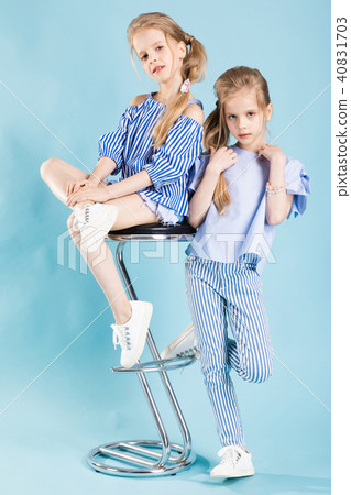 Girls twins in light blue clothes are posing near a bar stool on a blue background. Girls twins in light blue clothes are posing near a bar stool on a blue background. 40831703