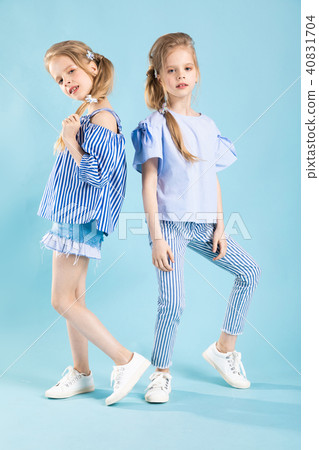 Girls twins in light blue clothes are posing on a blue background. Girls twins in light blue clothes are posing on a blue background. 40831704
