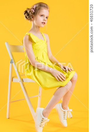 A girl is sitting on a white chair on a yellow background. 40831720