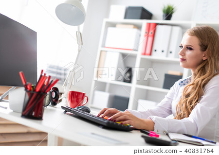 Beautiful young girl sitting at desk in office and working at computer. Before the girl there are Beautiful young girl sitting at desk in office and working at computer. Before the girl there are 40831764