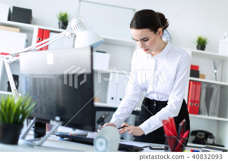 A young girl in the office is standing near the table, holding a pencil and a calculator in her hand 40832093