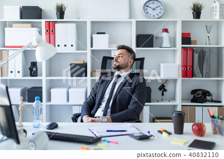 The man in the office at the table stooped to the back of the chair and looked out the window. 40832110