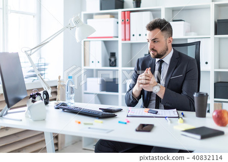 A man sits in a chair in the office at the table and looks at the monitor. A man sits in a chair in the office at the table and looks at the monitor. 40832114