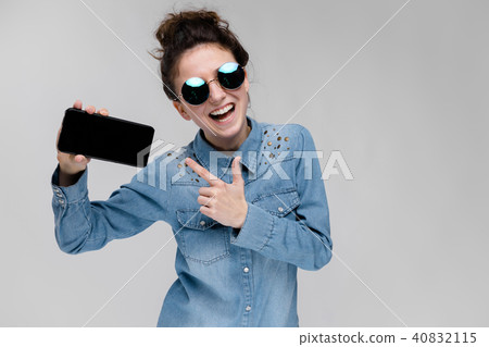 Young brunette girl in round glasses. Hairs are gathered in a bun. Girl with a black phone. 40832115