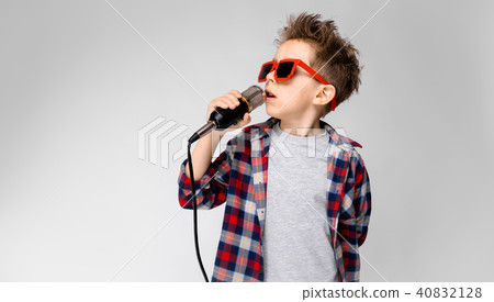 A handsome boy in a plaid shirt, gray shirt and jeans stands on a gray background. A boy wearing 40832128
