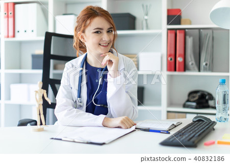 A beautiful young girl in a white robe is sitting at a table in the office. 40832186