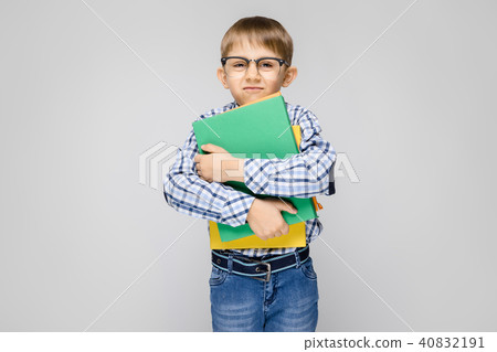 A charming boy with a vkletchatoy shirt and light jeans stands on a gray background. The boy holds A charming boy with a vkletchatoy shirt and light jeans stands on a gray background. The boy holds 40832191