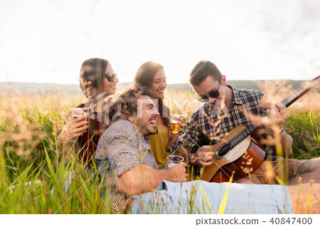 Young people sitting together in grass playing guitar 40847400