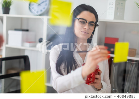A young girl stands near the board with stickers and holds a red cup and pencil in her hands. A young girl stands near the board with stickers and holds a red cup and pencil in her hands. 40849885