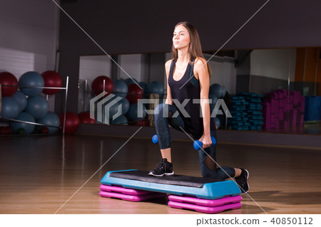 Young woman performs step cardio with dumbbells in a gym Young woman performs step cardio with dumbbells in a gym 40850112