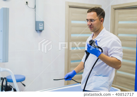 Proctologist holding an anoscope against a proctological chair. In the hospital Proctologist holding an anoscope against a proctological chair. In the hospital 40852717