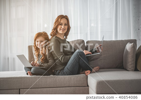 Mom and kid sitting with laptops and laughing at home Mom and kid sitting with laptops and laughing at home 40854086