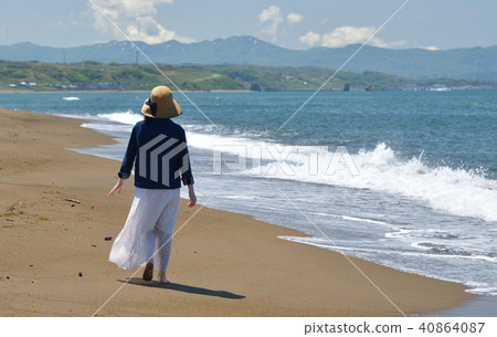 一個女人戴著草帽在沙灘上走在沙灘上的白色連衣裙的肖像 40864087