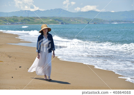 一個女人戴著草帽在沙灘上走在沙灘上的白色連衣裙的肖像 40864088