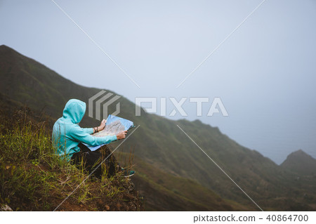 Traveler wear blue hoodie with the map sitting on the hill of a mountain in front of a gorgeous Traveler wear blue hoodie with the map sitting on the hill of a mountain in front of a gorgeous 40864700