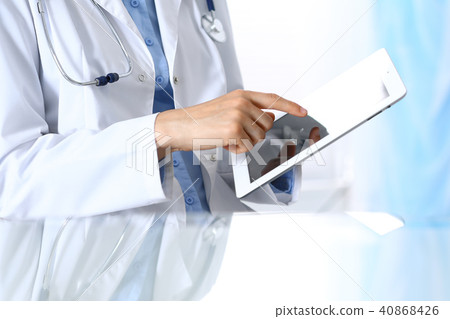 Woman doctor using tablet computer while sitting. Reflecting glass table is a working place of Woman doctor using tablet computer while sitting. Reflecting glass table is a working place of 40868426