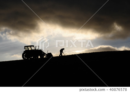 Silhouette of farmer working next to his tractor 40876578