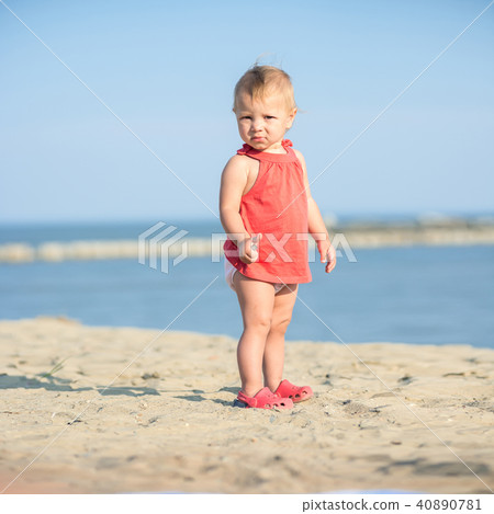 Baby girl in red dress playing on sandy beach near the sea. Baby girl in red dress playing on sandy beach near the sea. 40890781